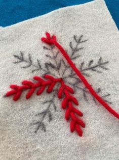 an embroidered snowflake on a piece of white fabric with red thread in the middle