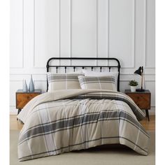 a bed with plaid comforter and pillows in a white room next to a wooden dresser