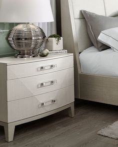 a bedroom with a bed, nightstand and lamp on the night stand in front of it