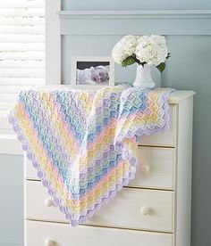 a crocheted blanket sitting on top of a dresser next to a vase with flowers