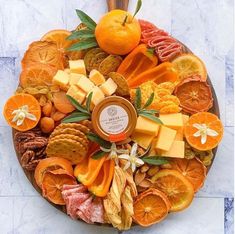 a platter filled with oranges, crackers and other food on top of a marble table