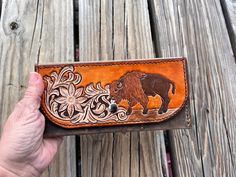 Carry your essentials in style with our Western Floral Bison 3 Card Ladies Clutch Wallet. Made in the traditional western floral style, painstakingly hand carved and hand painted design, this wallet is a one-of-a-kind piece. The hand painted bison adds a unique touch, while the hand stitching with brown leather thread ensures durability. Handcrafted in Texas with love and care. The body is hand crafted from a lighter colored, rustic oil tanned leather giving this wallet the already 'broken in' f Custom Brown Hand Tooled Wallets, Custom Hand Tooled Brown Wallet, Artisan Hand-tooled Bifold Wallet, Artisan Hand Tooled Bifold Wallet, Artisan Hand Tooled Wallets, Traditional Hand Tooled Wallets For Everyday Use, Artisan Hand-tooled Wallets For Gifts, Artisan Hand-tooled Wallets For Everyday Use, Artisan Hand Tooled Wallet For Everyday Use