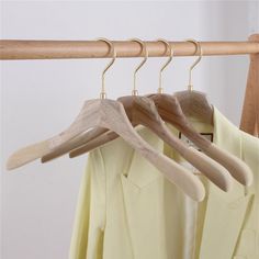 three wooden hangers are hanging from a coat rack with two shirts on it and one is yellow