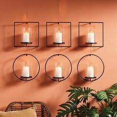 four candles are hanging on the wall next to a wicker chair and potted plant