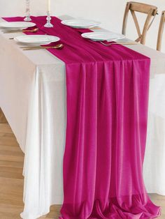 the table is set with white plates, silverware and fuchsia pink chiffon