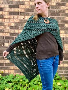 a woman standing in front of a brick wall wearing a green crocheted shawl