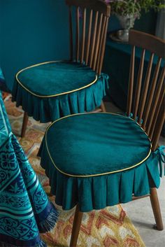 two wooden chairs with green covers on them in front of a blue wall and rug