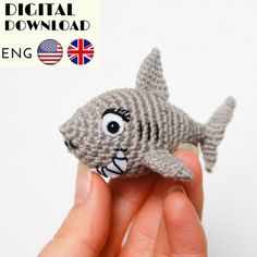 a hand is holding a small knitted toy shark in front of a white background