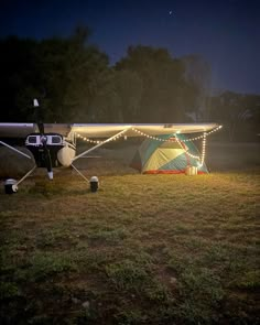 an airplane with lights on it parked in the grass near a tent and trees at night