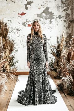 a woman in a black and white dress is standing on a runway with plants behind her