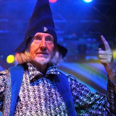 an older man wearing a black hat and blue vest giving the peace sign with his right hand