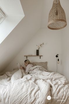 a woman laying in bed reading a book under a light fixture hanging from the ceiling