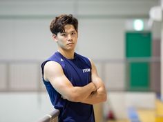 a young man is standing with his arms crossed and looking off to the side in an indoor gym