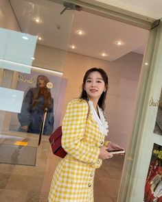 a woman standing in front of a store window holding a purse and looking at the camera