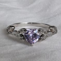 a ring with a heart shaped purple diamond surrounded by diamonds on a white cloth background