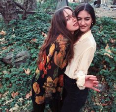 two young women hugging each other in the woods with leaves on the ground behind them