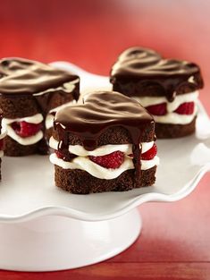 four chocolate desserts on a plate with white frosting and strawberries in the middle