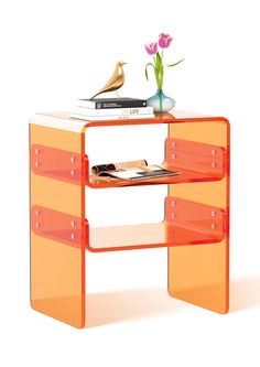 an orange shelf with some books and a vase on top of it next to a flower