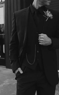 a man in a suit and tie standing next to a building with a flower on his lapel