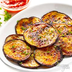 cooked eggplant slices on a white plate with ketchup and parsley