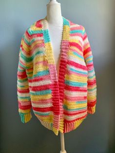 Handmade crocheted cardigan sweater is a vibrant stripe pattern. The long sleeves are trimmed with a ribbed cuff. The neck and bottom edge are also rib trimmed. Size is a generous medium. Made of acrylic yarn and machine washable. Reshape and lay flat to dry. Striped Sweater For Spring Layering, Spring Multicolor Knitted Cardigan, Spring Striped Chunky Knit Sweater, Striped Cardigan For Spring Layering, Cozy Striped Cardigan For Spring, Spring Striped Cardigan For Layering, Cozy Striped Spring Cardigan, Striped Oversized Cardigan For Spring, Colorful Knit Outerwear For Spring