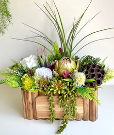 a wooden box filled with lots of different types of flowers and greenery on top of a white table