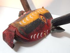 an old wooden bird with painted feathers on it's head and tail, sitting on a white surface