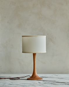 a wooden table lamp with a white shade on it's base, sitting on a marble surface