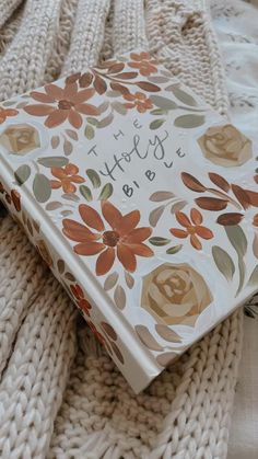 a book with flowers on it sitting on top of a white blanket next to a pile of blankets