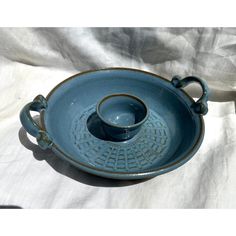 a blue pottery dish with handles on a white cloth