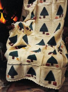 a crocheted christmas tree afghan sits in front of a fire place with a blanket draped over it