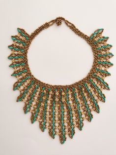 a gold and green necklace with beads on it's collarline is displayed against a white background