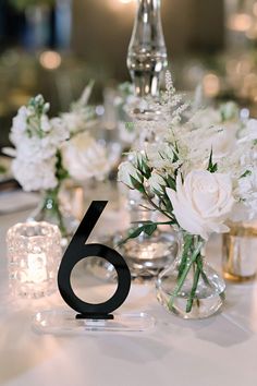 the table is set with candles and vases filled with white flowers, greenery and silverware