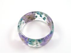 This handmade bangle bracelet features pressed lavender/purple Larkspur & Baby's Breath that are encased in transparent crystal clear resin and shaped into a unique and stylish bangle with a glassy finish that sparkles in the light. It is a chunky bangle with a curved profile; thicker in the center and tapering on the sides. This bangle embodies contemporary resin jewelry for the nature lover. The eco resin is crystal clear plant base resin, UV resistant, strong and environmentally safe. Each pi Blue Resin Bracelets For Gift, Blue Resin Bracelets As Gifts, Blue Resin Bracelets Perfect For Gifts, Blue Resin Bracelets For Gifts, Resin Bangle Jewelry For Gifts, Resin Bangle Jewelry Gift, Adjustable Clear Bangle Jewelry, Purple Bangle Bracelets As A Gift, Adjustable Clear Bangle Bracelet