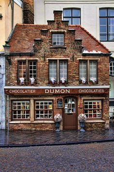 an old brick building with chocolate shops on the front and side windows, sitting next to a cobblestone street