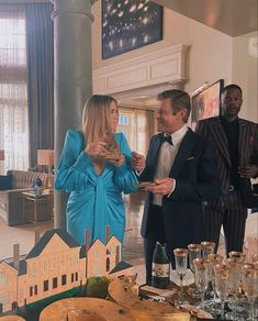 two men and a woman standing in front of a table full of wine glasses, cheeses and bread