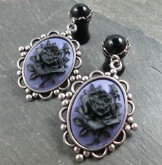 "These dangle plugs feature smooth round black gems, set in closed silver plated scalloped settings. Dangling from each is a pretty antiqued silver plated frame. The settings hold purple cameos with black roses. These would be perfect for a Gothic wedding or special occasion. These are available in the following sizes/styles: 12g (2mm) - Steel Screw Back 10g (2.4mm) - Steel Screw Back 8g (3mm) - Steel Screw Back 8g (3mm) - Acrylic Screw Back 8g (3mm) - Steel No Flare w/O Rings 6g (4mm) - Steel S Gothic Pierced Jewelry For Wedding, Handmade Gothic Wedding Earrings, Dangle Plugs, Black Gems, Acrylic Gems, Gauges Plugs, Plugs Earrings, Gothic Wedding, Black Acrylics