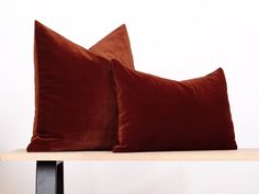 two brown velvet pillows sitting on top of a wooden table next to a white wall