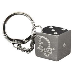 DIOR RHINESTONE GAMBLER DICE KEYRING KEYCHAIN The large square shiny reflective silver tone dice has the Dior name logo on two sides and the pips 1,2,3 and 5. Everything is set with bright clear rhinestones. A thick chain is attached to a round key holder that has a hinged lever closure. A larger size, the dice measures 1 inch square. The ring is 1 3/8 inch in diameter and the chain is 2 inches long. Color: Silver tone Material: metallic Marks: Brand mark Clasp Style: Year: 2004 Measures: 2 x 2 Dior Keychain, Accessory Inspo, Brand Mark, Inside My Bag, Silver Keychain, Cute Keychain, Essential Bag, Cute Little Things, Name Logo