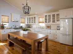 a large kitchen with white cabinets and wood flooring is pictured in this image, there are two benches at the center of the table