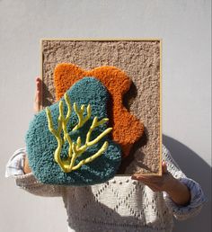 a woman holding up a piece of art made out of corals and seaweed