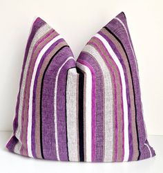 a purple and white striped pillow sitting on top of a white table next to a wall