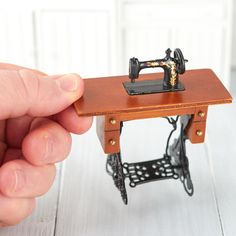 a miniature sewing machine sitting on top of a wooden table next to a person's hand