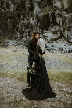 a man and woman standing next to each other in front of a rocky mountain area