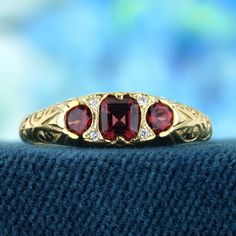 The ring features a vintage style, characterized by intricate carved detailing and a timeless aesthetic. The yellow gold setting offers a warm and rich backdrop for the gemstones. At the heart of the ring are three natural vibrant red garnets. Complementing the garnets are natural diamonds, round in shape and carefully placed to add sparkle and elegance. A perfect addition to any jewelry collection, this ring brings a touch of vintage charm to every special occasion. CHARACTERISTICS Status: Made to order Origin: Thailand Metal: Solid 9K Yellow Gold Ring Size: US 3-8 Total Gemstones Weight: 0.72 carat. (approx.) Total Gram Weight: 2.00 g. (approx.) *Pictures have been enlarged to show details* PRIMARY STONE(S) Stone: Natural Garnet Color: Red Shape: Oval Size: 4 x 3.5, 3 mm. Number: 3 Weigh Luxury Ruby Three Stone Rings, Luxury Three Stone Ruby Ring, Luxury Red Three Stone Jewelry, Luxury Red Three-stone Jewelry, Luxury Ruby Ring With Gemstone Accents For Anniversary, Luxury Three Stone Ruby Ring For Wedding, Fine Jewelry Yellow Gold Ruby Ring With Intricate Design, Gold Heirloom Ruby Ring With Gemstone Accents, Luxury Gold Three-stone Ruby Ring