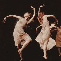 two women are jumping in the air with their arms outstretched and legs spread wide, wearing white dresses