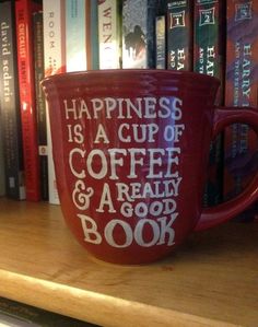 a red coffee cup sitting on top of a wooden table next to bookshelves