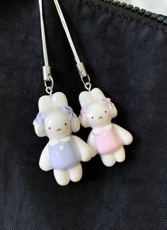 two white teddy bears with pink and blue dresses are hanging from a pair of lanyards