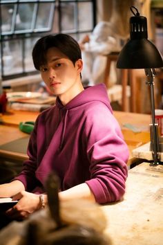 a young man sitting at a desk in front of a lamp