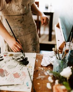 a woman is painting on an easel with paintbrushes in front of her